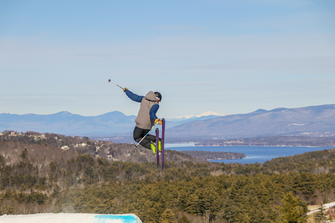Skier jumping in front of mountains and lake.
