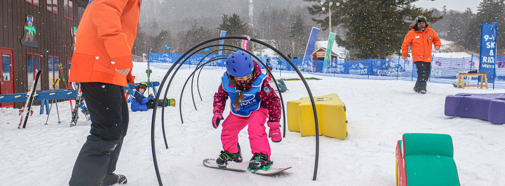Instructor helps child snowboard under hoops.